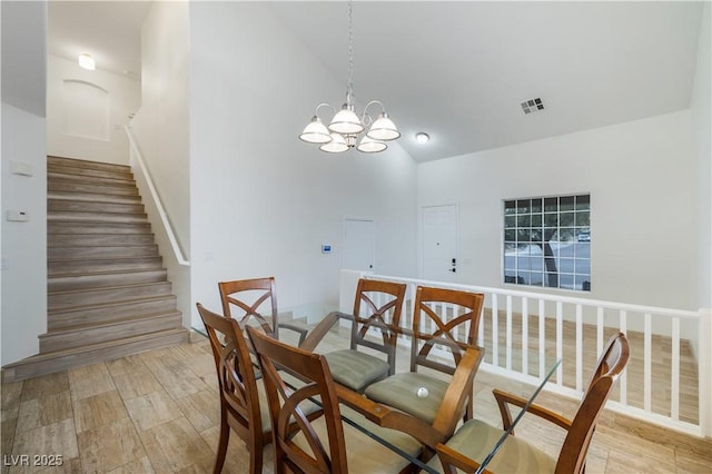 dining area featuring visible vents, high vaulted ceiling, light wood-style flooring, a chandelier, and stairs