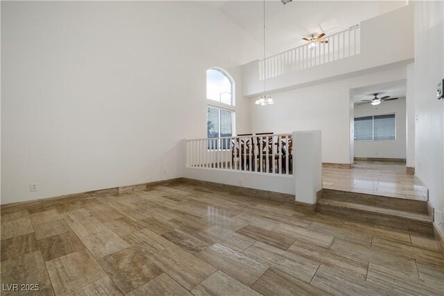 unfurnished room with ceiling fan with notable chandelier, baseboards, and a towering ceiling