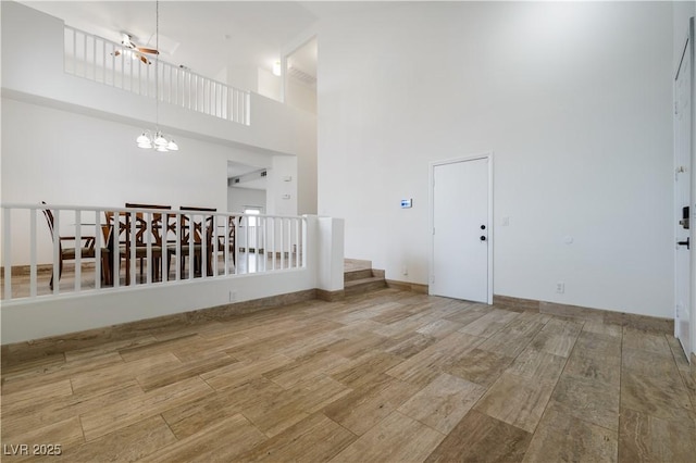 spare room with wood finish floors, an inviting chandelier, a towering ceiling, and stairs