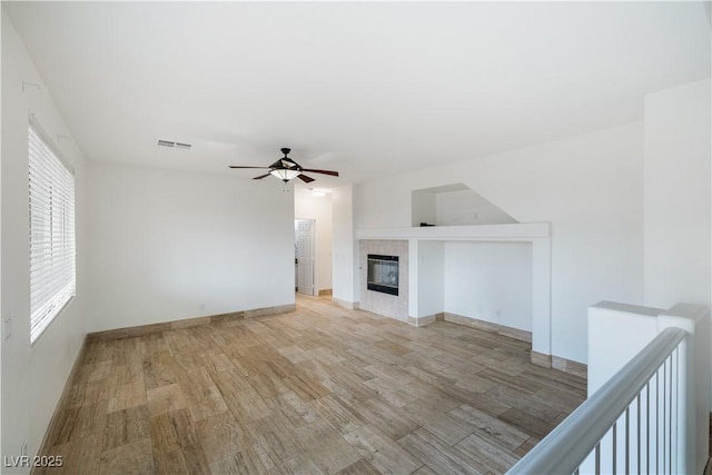 unfurnished living room featuring baseboards, visible vents, light wood finished floors, ceiling fan, and a tiled fireplace