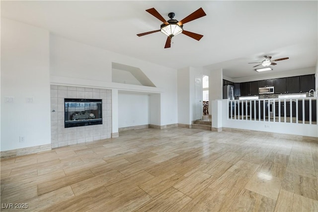 unfurnished living room featuring a tile fireplace, baseboards, light wood-type flooring, and a ceiling fan