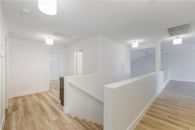 corridor with visible vents, an upstairs landing, baseboards, and light wood finished floors