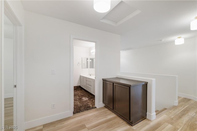 hallway with a sink, light wood-type flooring, baseboards, and attic access