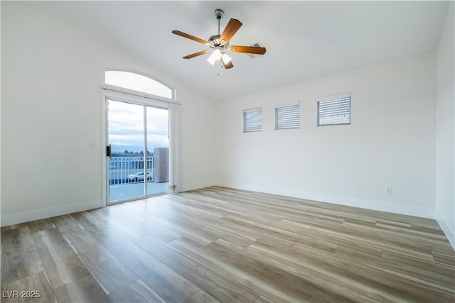 spare room featuring light wood finished floors, baseboards, ceiling fan, and vaulted ceiling