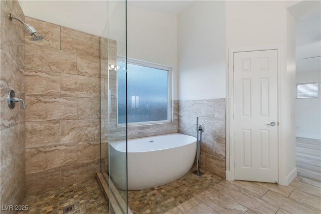 full bath with a wainscoted wall, tiled shower, tile walls, and a freestanding tub