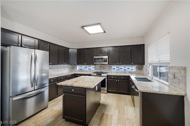 kitchen with light stone countertops, a sink, decorative backsplash, appliances with stainless steel finishes, and a center island