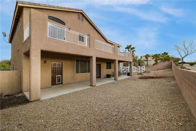 back of house featuring a balcony, a patio area, a fenced backyard, and stucco siding