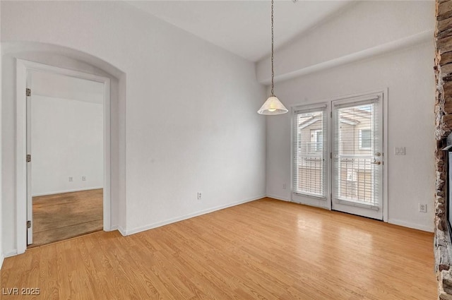 empty room with baseboards, lofted ceiling, and light wood finished floors