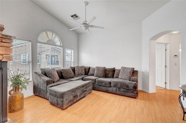 living area with visible vents, high vaulted ceiling, arched walkways, light wood-style floors, and ceiling fan