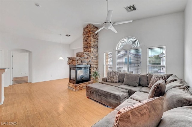 living area featuring a stone fireplace, light wood-style floors, visible vents, and arched walkways