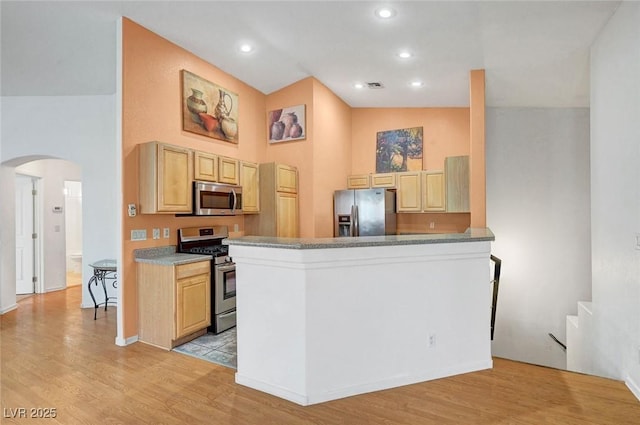 kitchen with light wood-style flooring, light brown cabinets, arched walkways, and appliances with stainless steel finishes