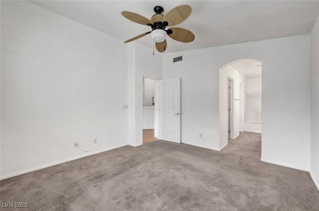 carpeted empty room with a ceiling fan, arched walkways, visible vents, and baseboards