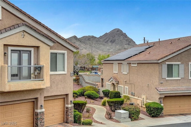 exterior space featuring stucco siding, stone siding, a mountain view, solar panels, and a tiled roof