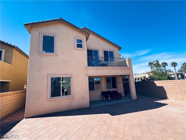 back of property with a balcony, stucco siding, a patio, and fence