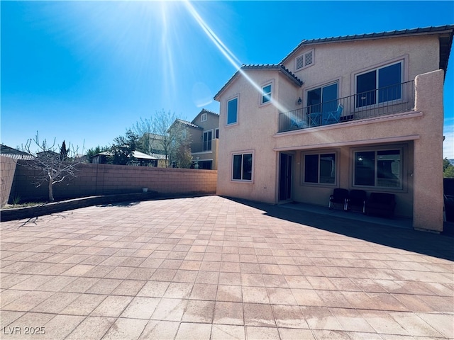 rear view of house with a patio, a balcony, fence private yard, and stucco siding