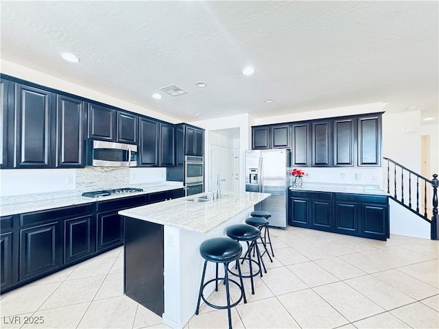 kitchen with a kitchen bar, light stone counters, a sink, stainless steel appliances, and light tile patterned floors