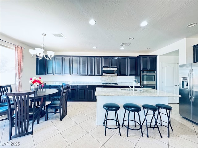 kitchen with visible vents, a sink, a breakfast bar, appliances with stainless steel finishes, and a kitchen island with sink