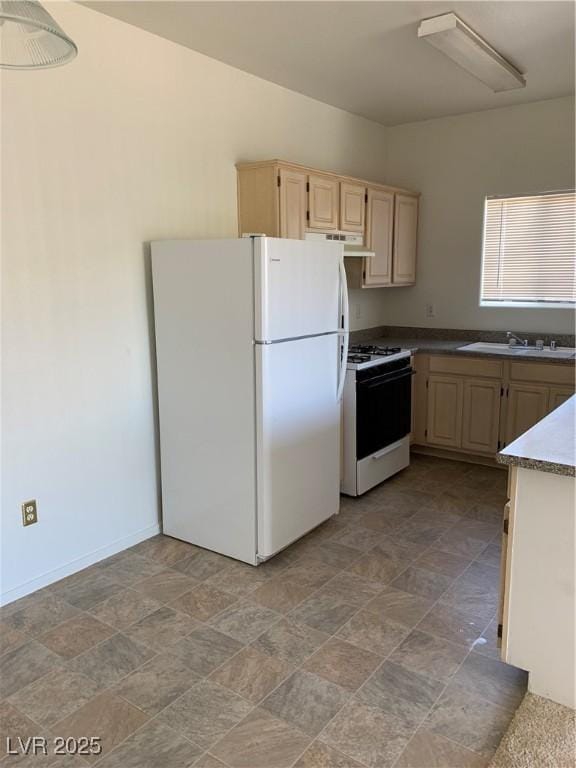 kitchen with light brown cabinetry, a sink, stone finish flooring, white appliances, and baseboards