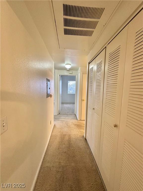 corridor with visible vents, light carpet, baseboards, and attic access