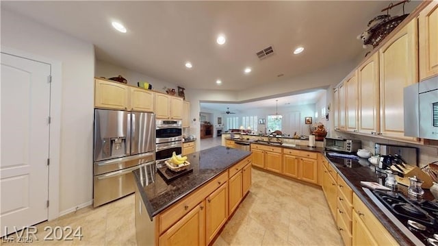 kitchen with a kitchen island, light brown cabinetry, dark stone counters, a peninsula, and stainless steel appliances