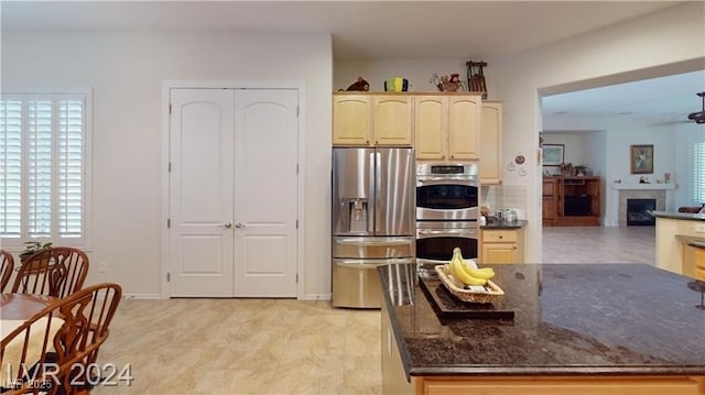 kitchen featuring dark stone countertops, appliances with stainless steel finishes, a fireplace, baseboards, and ceiling fan