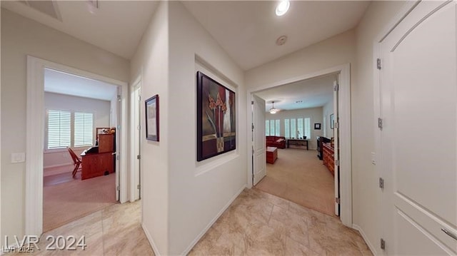 hallway with baseboards and light colored carpet