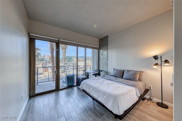 bedroom featuring baseboards, wood finished floors, access to exterior, and a view of city