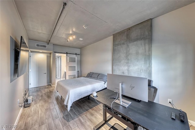 bedroom featuring a barn door, wood finished floors, visible vents, and baseboards