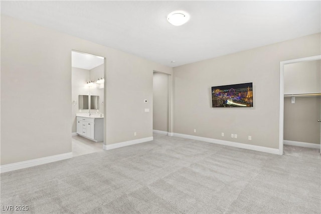 unfurnished bedroom with a spacious closet, connected bathroom, baseboards, light carpet, and a closet