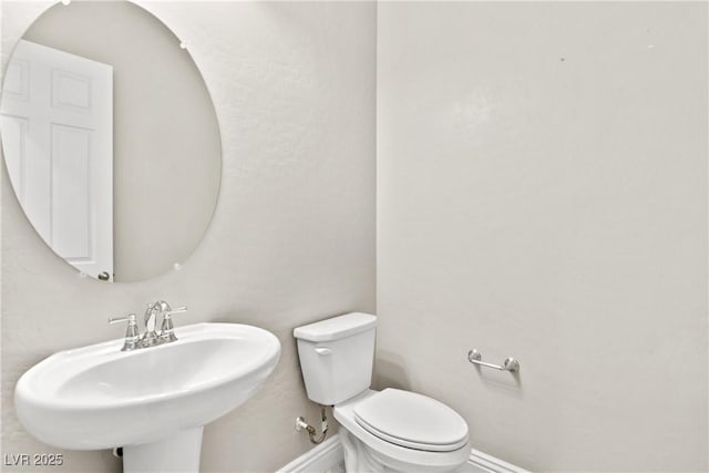 half bath with toilet, baseboards, and a sink