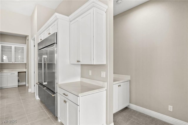 kitchen featuring baseboards, light countertops, stainless steel built in fridge, light tile patterned flooring, and white cabinets