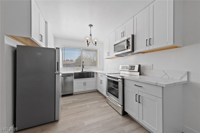 kitchen featuring light stone counters, a sink, white cabinets, appliances with stainless steel finishes, and light wood-type flooring