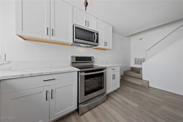 kitchen featuring light wood finished floors, white cabinets, stainless steel appliances, and light stone counters