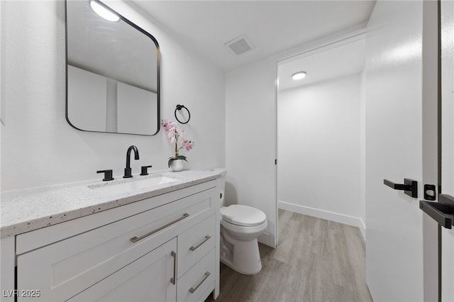 bathroom featuring visible vents, baseboards, toilet, wood finished floors, and vanity