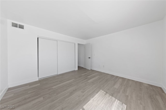 unfurnished bedroom featuring light wood-type flooring, visible vents, baseboards, and a closet