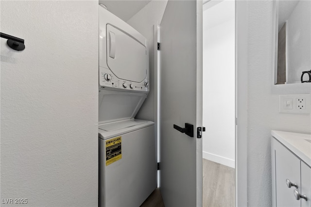 laundry room with baseboards, stacked washer and clothes dryer, wood finished floors, and laundry area