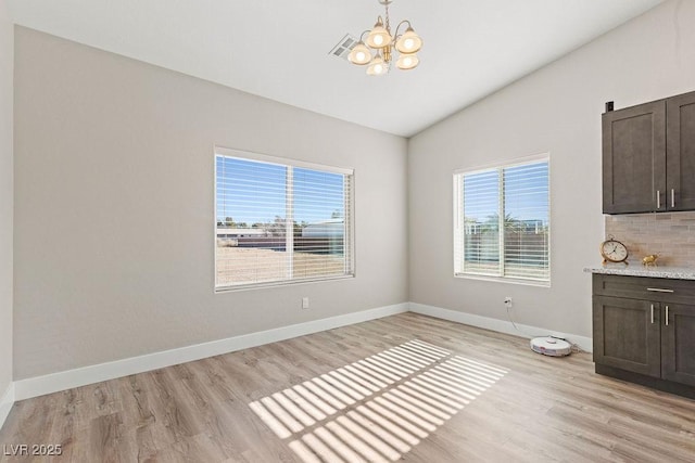 unfurnished dining area featuring a wealth of natural light, baseboards, lofted ceiling, and light wood-style flooring