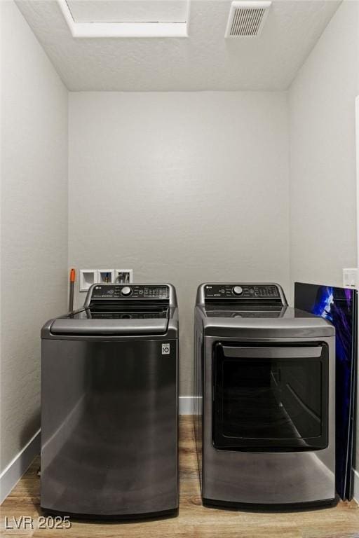 clothes washing area featuring washer and dryer, visible vents, wood finished floors, and laundry area