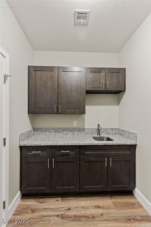 kitchen with baseboards, visible vents, a sink, dark brown cabinetry, and light wood-style floors