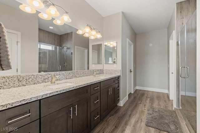 bathroom with a shower stall, baseboards, double vanity, wood finished floors, and a sink