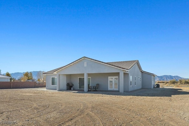 rear view of property with a mountain view, stucco siding, french doors, and fence