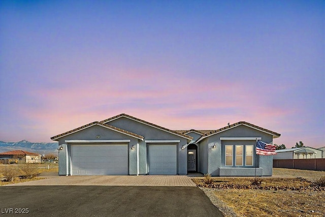 ranch-style home featuring fence, a garage, driveway, and stucco siding