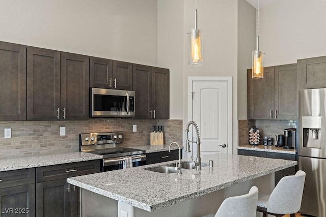 kitchen featuring light stone countertops, a sink, stainless steel appliances, dark brown cabinets, and a kitchen bar