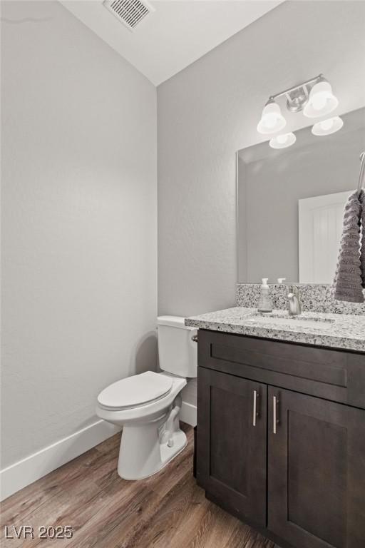 half bathroom featuring visible vents, toilet, wood finished floors, and vanity