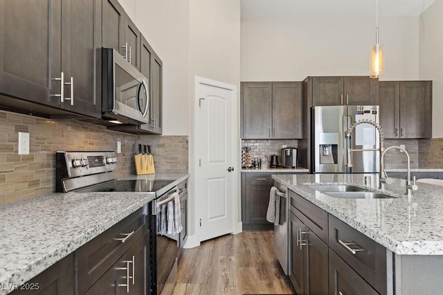 kitchen featuring light stone countertops, wood finished floors, a sink, dark brown cabinets, and appliances with stainless steel finishes