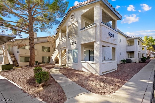 view of property exterior featuring stucco siding, a tile roof, a residential view, central AC unit, and stairs