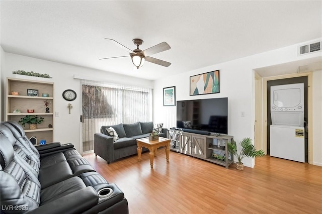 living area featuring light wood finished floors, visible vents, stacked washer / drying machine, and ceiling fan