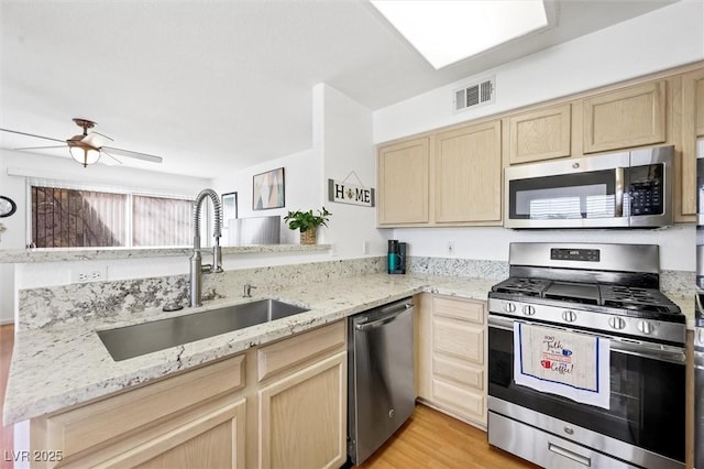 kitchen with visible vents, light brown cabinetry, light stone counters, stainless steel appliances, and a sink