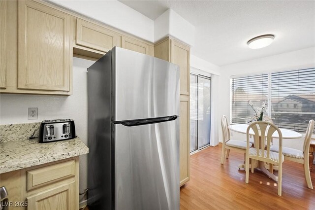 kitchen with light brown cabinetry, light wood-type flooring, freestanding refrigerator, and light stone counters