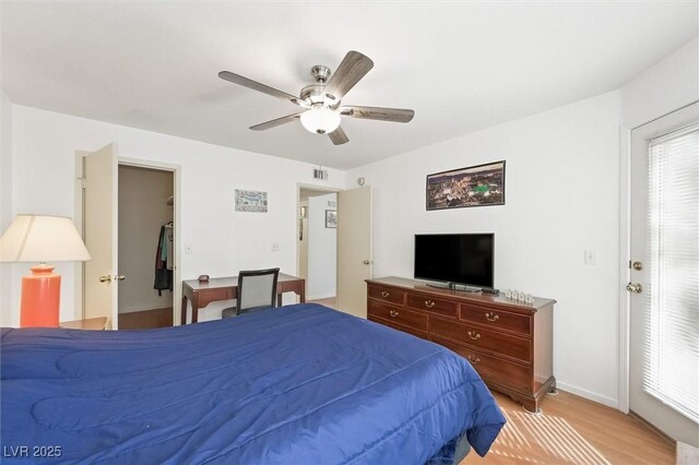 bedroom with baseboards, visible vents, light wood-style flooring, ceiling fan, and a walk in closet